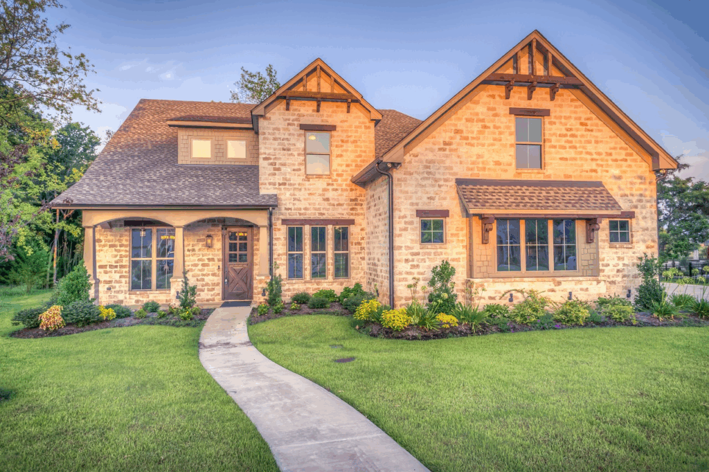 Front view of a stone house with a curved concrete walkway leading to the front door and a manicured lawn.